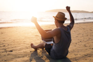 Young male businessman putting hands up for success on tropical summer beach - it indicates freedom such as financial freedom or remote work concept
